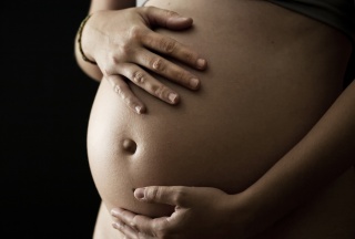 Schwangere Frau umfasst liebevoll ihren Bauch