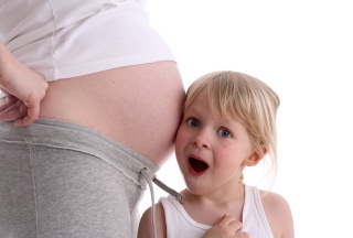 Geschwister horcht am Bauch der schwangeren Mutter
